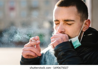 Smoking. Closeup Man With Mask During COVID-19 Pandemic Coughing And Smoking A Cigarette At The Street. Smoking Causes Lung Cancer And Other Diseases. The Dangers Of Smoking. Coronavirus.