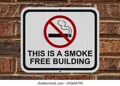 Smoking Free Building Sign, An Red And White Sign With Cigarette Icon And Not Symbol With Text On A Brick Building