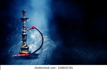 Smoking a hookah on a dark concrete field, in clouds of smoke and neon light