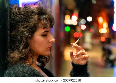 Smoking latin woman standing with a cigarette in her hand on the street at night. - Powered by Shutterstock