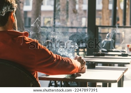 Smoking man. Back view of man smoking tobacco cigarette in cafe. Unhealthy lifestyle. 
