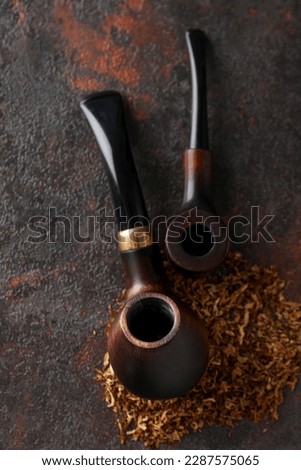 Smoking pipes with tobacco on dark textured background