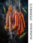 Smoking vertically hanging sausages. 
Clouds of smoke rise up and envelop the sausages hanging in a row. Dark background with flying green rosemary leaves