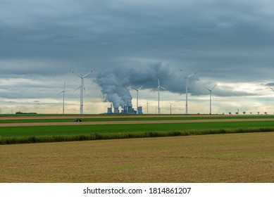 Smoky coal-fired power plant with wind turbines in a field