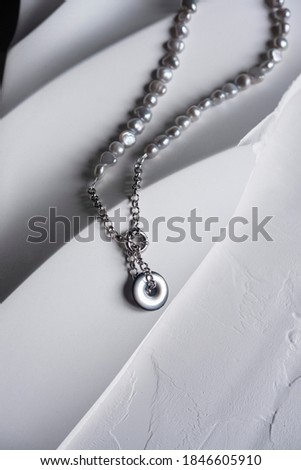 Smoky gray pearl necklace with ash gray mother-of-pearl pendant in the form of a ring on a silver chain. The piece of jewelry lies on a white plaster plate and is a wonderful piece of jewelry Vertical