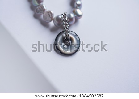 Smoky gray pearl necklace with ash gray mother-of-pearl pendant in the form of a ring on a silver chain. The piece of jewelry lies on a white plaster plate and is a wonderful piece of jewelry.