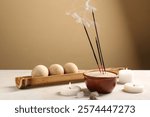 Smoldering incense sticks, burning candles and wooden massage balls on light table against color wall