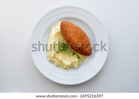 Smooth bed of mashed potatoes topped with golden fried croquette and sprig of microgreens, presented on a clean white plate. Warm, comforting, and restaurant-style, ideal for food photography.