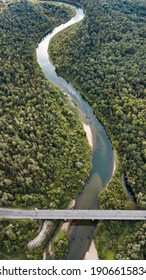 Smooth bends of the river flowing through the green forest. The banks of the river are connected by a road bridge