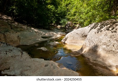 A Smooth Bizarre Channel In The Rock Cut By The Mountain River At The Bottom Of The Crimean Canyon. Transparent Water In The Shade Flows Over A Smooth Yellow Monolith. Crimea.