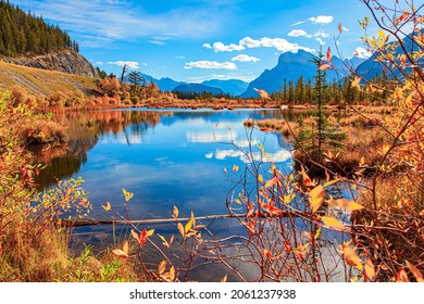  The smooth cold water of Lake Vermillon reflects the snow-white clouds. Indian summer in the Rocky Mountains. Red, yellow and orange foliage of the autumn forest. Canada