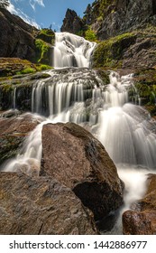 Smooth flowing waterfall cascading down rocks with vibrant green moss growing on them. Flatrock falls, Newfoundland.  