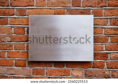 A smooth metal panel is affixed to an old brick wall, showcasing the contrast between the shiny surface and the rough, textured bricks underneath. This urban backdrop creates a striking visual.