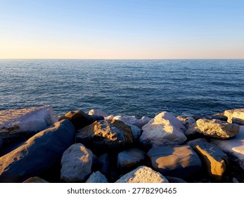 Smooth ocean waves gently lap against a rocky shoreline during a serene sunset. Warm golden light bathes the scene, creating a peaceful and tranquil atmosphere. This image evokes feelings of calm, ref