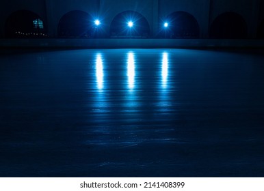 Smooth, Shiny Surface Of An Ice Rink With Reflected By Spotlights. Dark Empty Ice Arena With Soft Blue Light. Concept Of Winter Sports Games, Hockey, Figure Skating. Icy Background Of Slippery Ice.