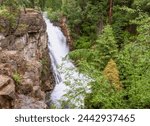 Smooth silky waterfall in luscious green forrest on one side and brownish rock bluff on the other