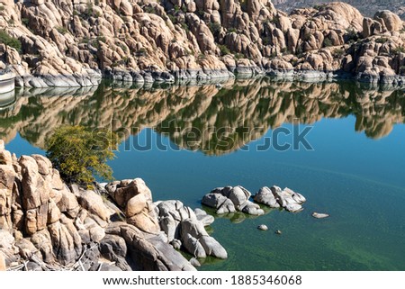 Smoothed giant granite boulders frame the edge of Watson Lake Reservoir near Prescott, Arizona. The landscape is reflected in the perfect mirror surface of the water. Water levels are marked in grey.