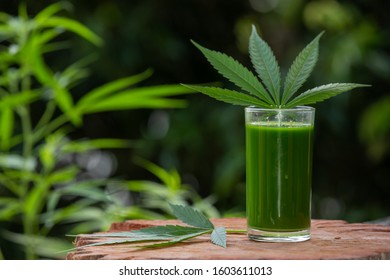 Smoothie cannabis juice that is placed on a wooden floor and has a natural green background.