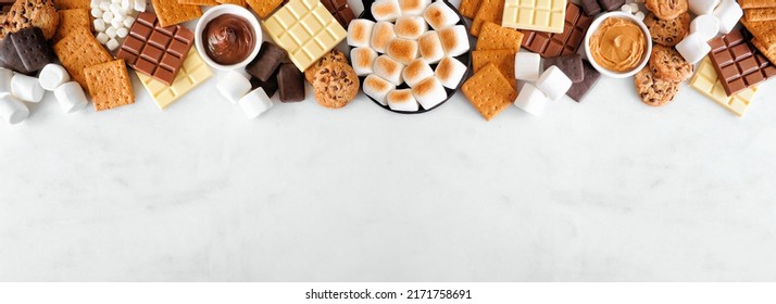 Smores Buffet Top Border. Roasted Marshmallows, Crackers, Chocolate And A Group Of Ingredients. Overhead View Over A White Marble Background.