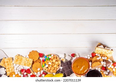 S'mores Home Party Food And Ingredients. Smores Buffet Background With Various Marshmallow, Crackers, Chocolate, Fruits, Chocolate, Toppings, Sauces. Traditional Autumn Summer American Smores Dessert 