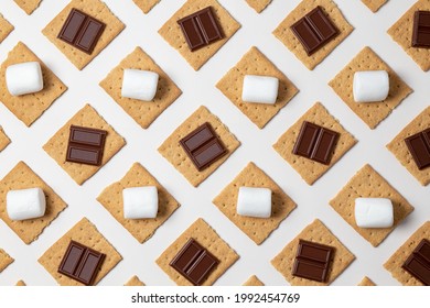 s'mores ingredients. graham cracker squares with chocolate bars, marshmallows on a white background. 