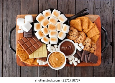 Smores platter. Roasted marshmallows, crackers, chocolate and a group of ingredients. Above view on a dark wood background.