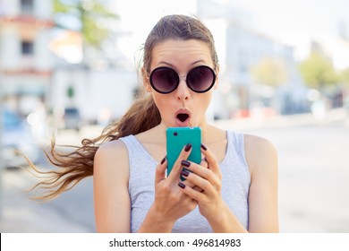 SMS. Closeup Portrait Funny Shocked Anxious Scared Young Girl Looking At Phone Seeing Bad News Photos Message With Disgusting Emotion On Face Isolated Cityscape Background. Human Reaction, Expression