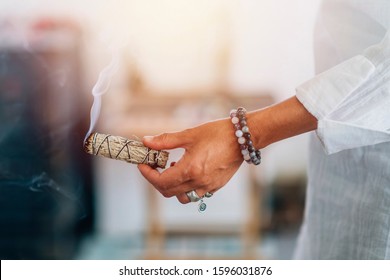 Smudging - Mãos de uma mulher espiritual segurando um bastão de borrão de sálvia fumegante