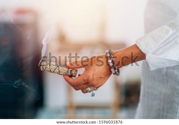 Smudging - Hands of a spiritual woman holding\
burning smoking sage smudge\
stick
