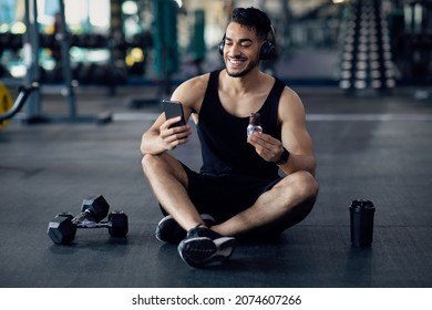 Snack Break. Smiling Young Arab Man Resting At Gym After Training, Middle Eastern Male Athlete Using Smartphone And Eating Protein Bar While Relaxing After Successful Sport Workout, Copy Space - Shutterstock ID 2074607266