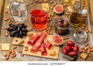 Snack food. Jamon and figs on board. Olives in glass jars. Glass of rose wine and sprig of grapes. Nuts and cheese. Rusty background. - Powered by Shutterstock