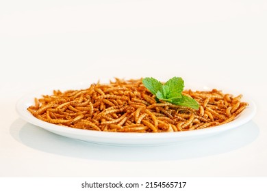 Snack insect isolated on white plate with mint decoration. Mealworms crustaceans tenebrio molitor, freeze-dried for snacking. Fried worms. Roasted mealworms