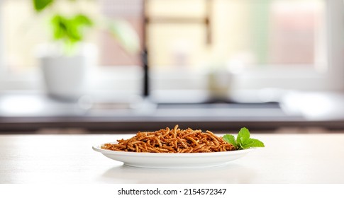 Snack insect on white plate with mint decoration and Kitchen Background. Mealworms crustaceans tenebrio molitor, freeze-dried for snacking. Fried worms. Roasted mealworms
