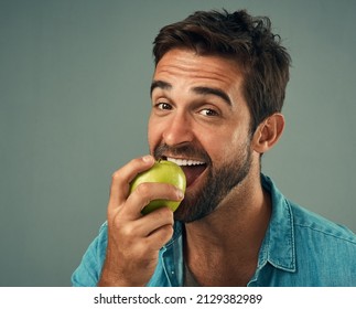 Snacking The Healthy Way. Studio Portrait Of A Handsome Young Man Eating An Apple Against A Grey Background.