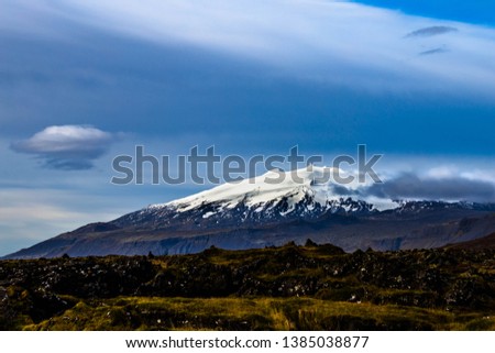 Snaefellsjokull Glacier on the Snaefellsnes Peninsula in Iceland. Small clouds move across its snow covered summit while snow fills in some of the ancient lava run lines down its side in autumn