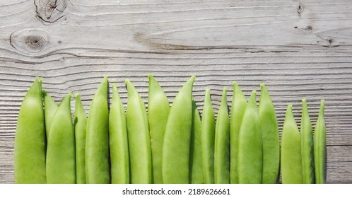 Snap Peas On Wood Background Or Table. Many Fresh Green Pea Pod Shells Just Picked From Garden. Pea Harvest Season From Garden. Sugar Pea, Snap Pea Or Pisum Sativum Var Plant. Selective Focus On Pod.