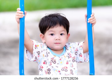 Snapshot of an Asian little child boy holding a blue swing. Children are playing on the playground in the evening. In the summer or spring. Hot and sweaty on the face. Child 2 years old.