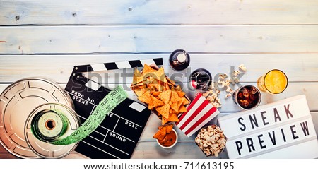 Sneak film preview panorama banner concept with cinema tickets, reels, nachos, popcorn, clapper boars, beer and fruit juice or cocktails on wood with copy space