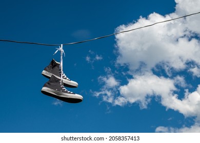 Sneakers hanging on electric wires against a background of blue sky and white clouds. - Powered by Shutterstock