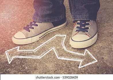 Sneakers on asphalt road with opposite arrows. Dilemmas concept.