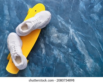 Sneakers and skateboard on color background