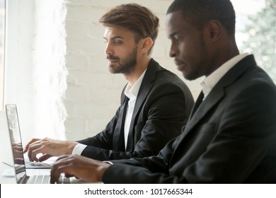 Sneaky Curious Caucasian Businessman Secretly Looking At Laptop Screen Of African Colleague Stealing Idea, White Office Corporate Spy In Suit Copying Work Of Black Coworker, Rivalry At Workplace