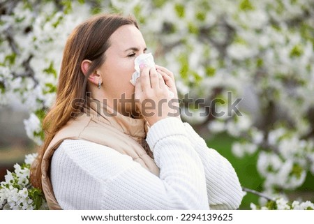 Sneezing woman with a nose wiper among the flowering trees in the park