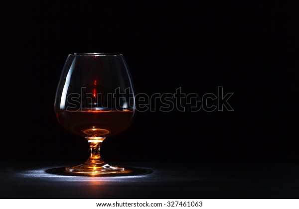 Snifter with brandy on\
black wooden table