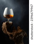 Snifter of brandy on a old wooden snag. Black background with copy space. Selective focus.