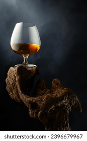 Snifter of brandy on a old wooden snag. Black background with copy space. Selective focus.