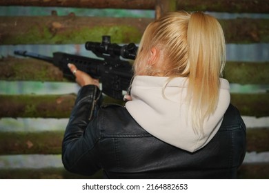 A Sniper Girl Aims With A Rifle From A Wooden House In The Forest.