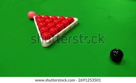 A snooker table with red balls in a triangle and a black and pink ball