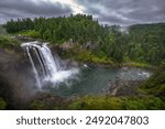 Snoqualmie Falls cascading into river under a cloudy sky in Washington State. Snoqualmie Falls is a 268-foot waterfall on the Snoqualmie River between Snoqualmie and Fall City.