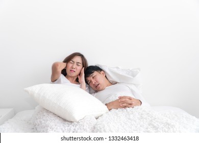 Snoring Asian Man And Young Asian Young Woman. Couple Sleeping In Bed. Young Girl Can't Sleep Because Of Her Man's Snoring. Man Snoring While His Wife Is Covering Ears With The Pillow.